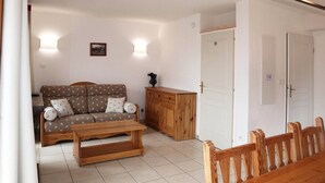 Un salon comprenant un canapé, une table basse en bois et un meuble. Il y a deux portes et un luminaire fixé au mur.