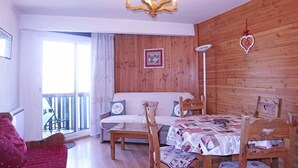 Una habitación acogedora con una pared de madera, un candelabro, una mesa de comedor con mantel a cuadros y un sofá con cojines.