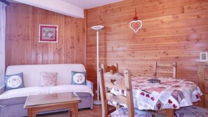 Una habitación acogedora con un muro de madera, un sofá blanco con cojines estampados, una mesa de comedor de madera con mantel a cuadros y una decoración en forma de corazón colgada.