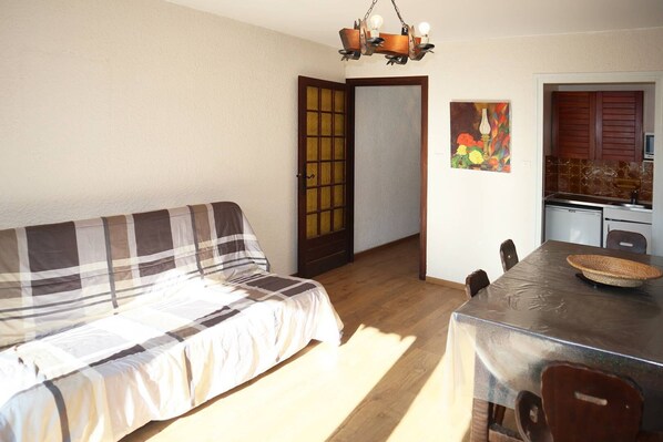 Ein gemütliches Zimmer mit einem Bett, einem Esstisch mit Stühlen, einer Küchenzeile und einem Bild an der Wand.