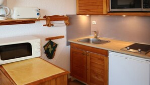 Una cocina compacta con armarios de madera, un microondas, un lavamanos y un refrigerador pequeño.