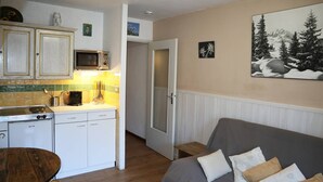 Una cocina compacta con microondas, estufa y pileta, una mesa de comedor de madera, y un sofá gris con almohadones.