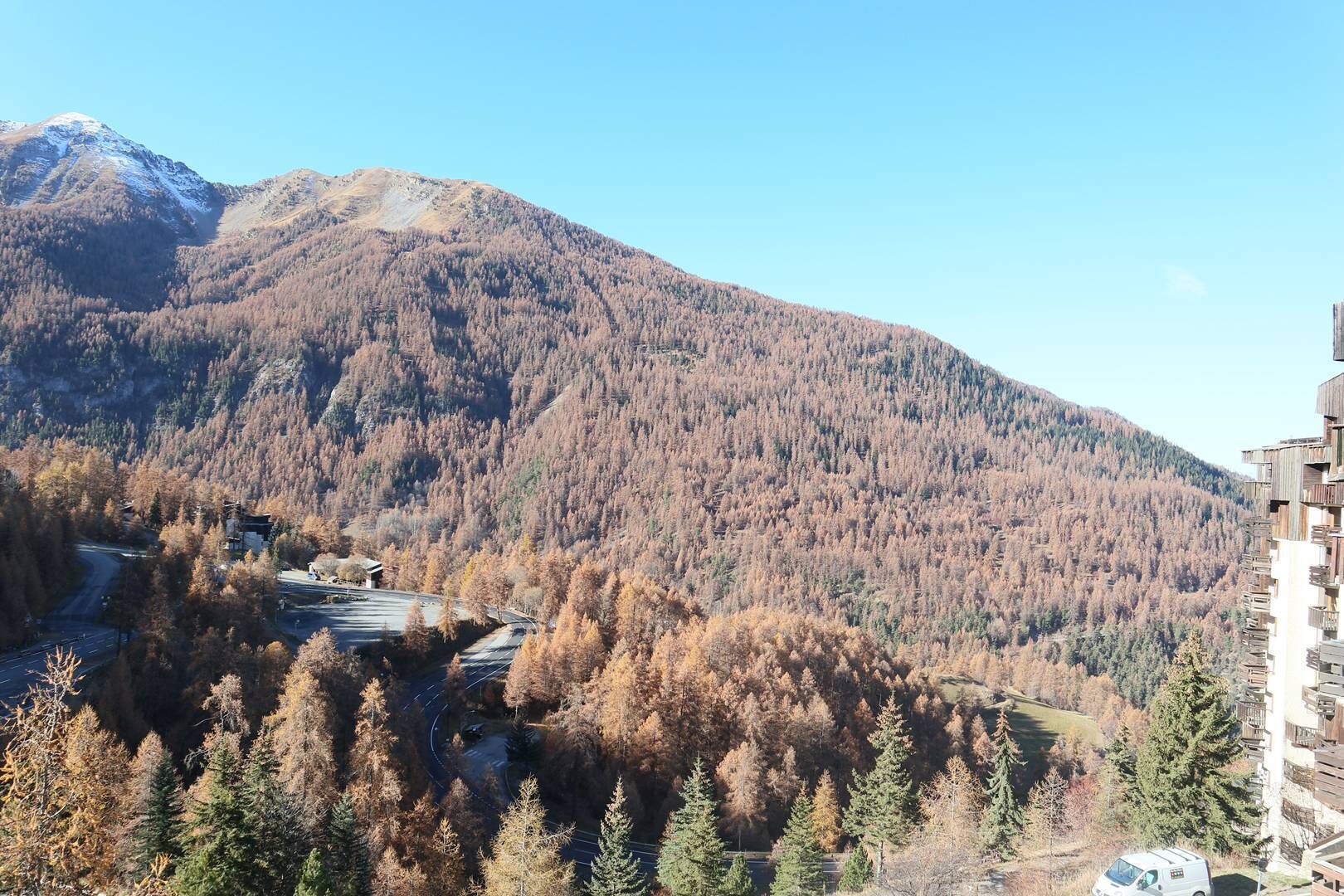Eine gebirgige Landschaft mit einer Straße, die zu einem Gebäude mit mehreren Balkonen führt.