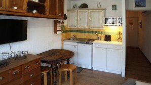 Una cocina compacta con armarios de madera, una mesa con taburetes, un microondas y un fregadero.