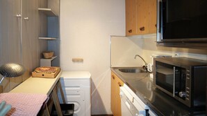 A compact kitchen with a microwave, sink, and a small stove. - Appartement Spacieux, Idéal Pour une Famille (LES ORRES 1650)