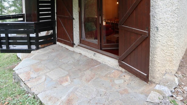 A stone-paved patio leading to a building with wooden shutters and a black fence. - Appartement Spacieux, Idéal Pour une Famille (LES ORRES 1650)