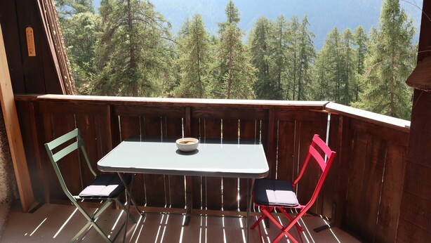 A balcony with a table and two chairs, overlooking a forest and mountains. - 2 Pièces 6 Personnes en Cœur de Station (LES ORRES 1650)