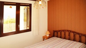 Une chambre à coucher comprenant un lit, une table de chevet, une lampe, une fenêtre avec des rideaux et un mur orné de lignes verticales.