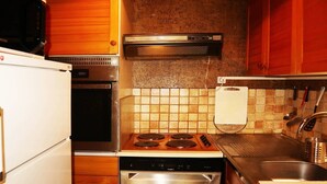 Une cuisine compacte équipée d’un four à micro-ondes, d’un four, d’une cuisinière, d’un lave-vaisselle et d’un dosseret carrelé.