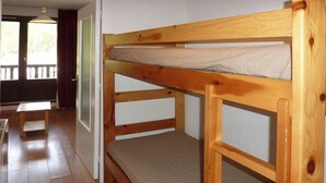 A bunk bed with a wooden frame and a mattress in a room with wooden flooring and a window with curtains. - Studio SUR LES Pistes (LES ORRES 1650)
