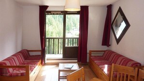 A cozy room with two striped sofas, a wooden table, and a large window with curtains.