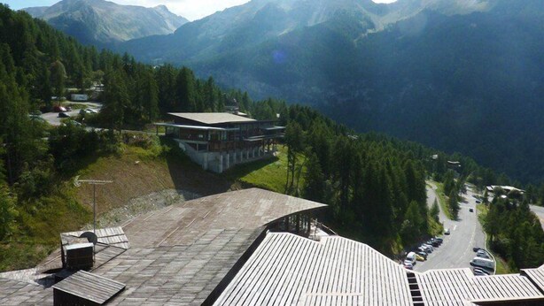A mountain lodge with a large wooden deck and a view of the surrounding mountains.
