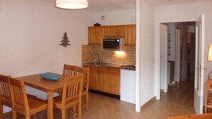 A compact kitchen with wooden cabinets, a microwave, and a sink. There is a dining table with chairs and a small blue bowl.