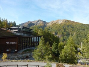 A modern building named 'Patinoire' with a glass facade, surrounded by a mountainous landscape.