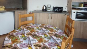 A small kitchen with a dining table covered with a tablecloth, a coffee maker, a microwave, and a TV on the wall. - 603 Balcon des Orres (LES ORRES 1650)
