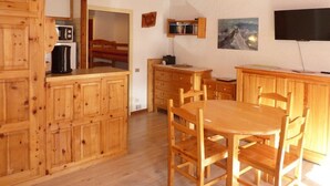 Une cuisine en bois avec une table et des chaises, un four à micro-ondes, une machine à café et un téléviseur à écran plat fixé au mur.
