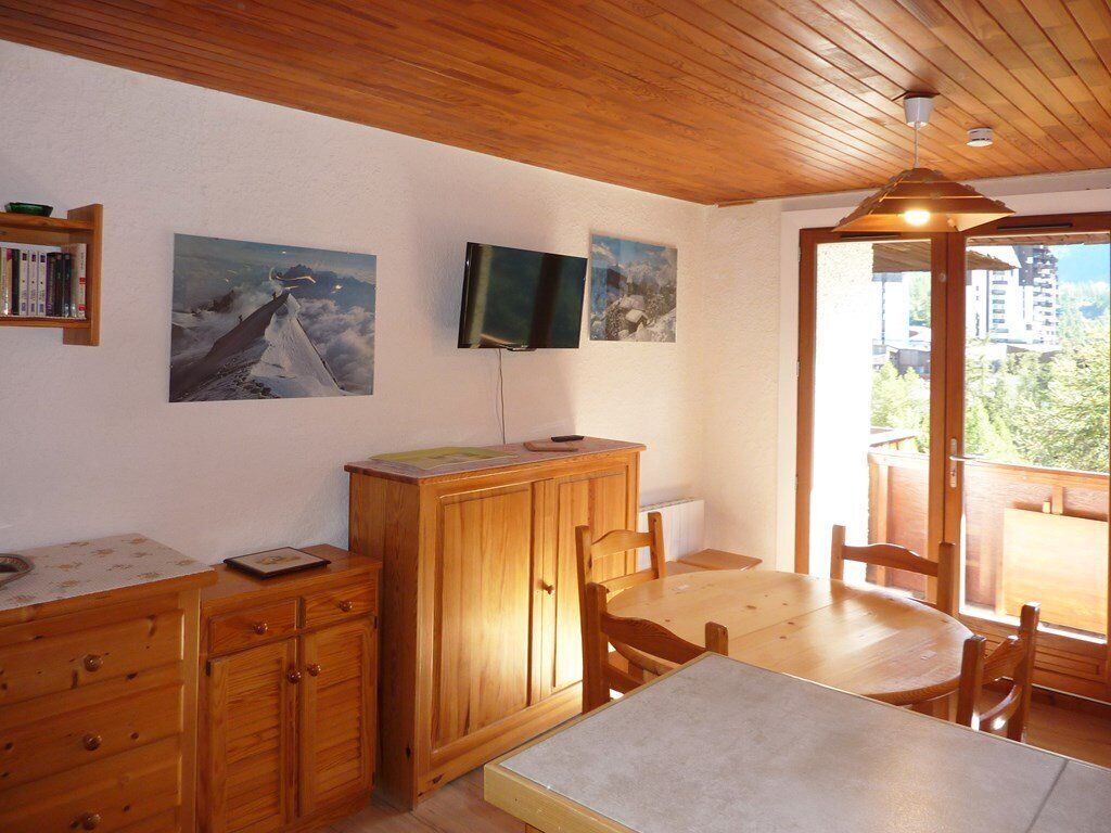 Een houten eetgedeelte met een tafel, stoelen, een kast en een aan de muur bevestigde televisie.
