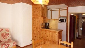 Une table à manger en bois avec quatre chaises, un buffet en bois et un coin cuisine équipé d’un four à micro-ondes et d’une machine à café.