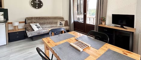 A cozy living area with a sofa, a dining table with placemats, a television, and a clock on the wall.