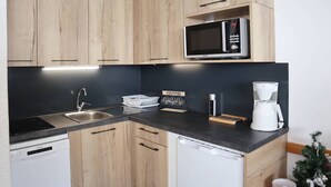 Una cocina moderna con armarios de madera, un lavamanos de acero inoxidable, un microondas, una cafetera y un escurreplatos.