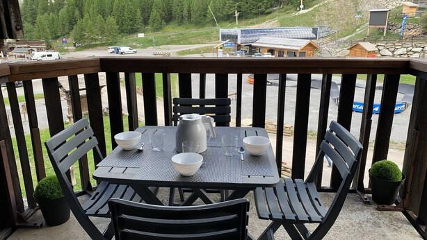 Un balcón con una mesa dispuesta para cuatro personas, con vista a una zona montañosa que incluye un telesilla y edificios.