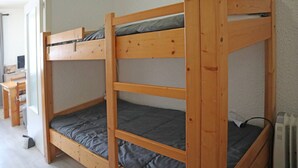 Una cama litera de tres niveles, un escritorio y una silla en una habitación con paredes blancas y un radiador.