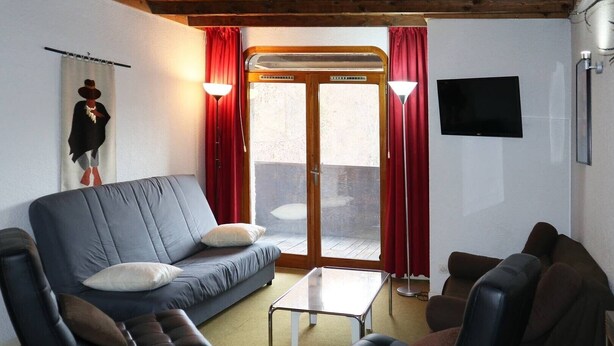 Una sala de estar con sofá, sillones, una mesa de centro, televisor y puerta corrediza de vidrio que da a un área exterior.