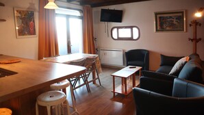 A cozy living room with a wooden dining table, bar stools, a sofa, and a TV mounted on the wall. - 2 Pièces 6 Personnes (LES ORRES 1650)