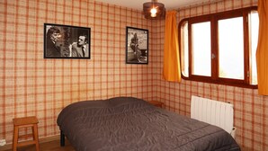 A bedroom with plaid wallpaper, a bed, a small stool, and two framed pictures on the wall. - 2 Pièces 6 Personnes (LES ORRES 1650)