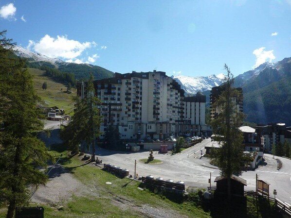 A multi-story hotel with a parking lot in front, surrounded by mountains and trees.