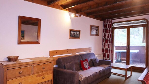 A cozy room with a wooden ceiling, a wooden bench, a cushioned bench, a wooden dresser, and a window with curtains. - Appartement N°22 Eperviere (LES ORRES 1650)