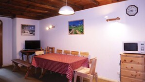 A dining area with a wooden table and chairs, a television, and a clock on the wall. - Appartement N°22 Eperviere (LES ORRES 1650)
