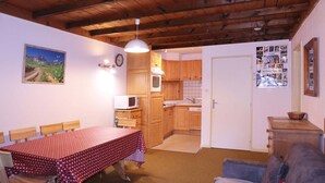 A cozy kitchen with wooden cabinets, a microwave, and a dining area with a checkered tablecloth. - Appartement N°22 Eperviere (LES ORRES 1650)