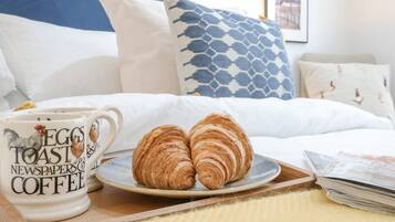 Una cama bien hecha con un cabecero azul, un plato con croissants y una taza con diseño de gallo.