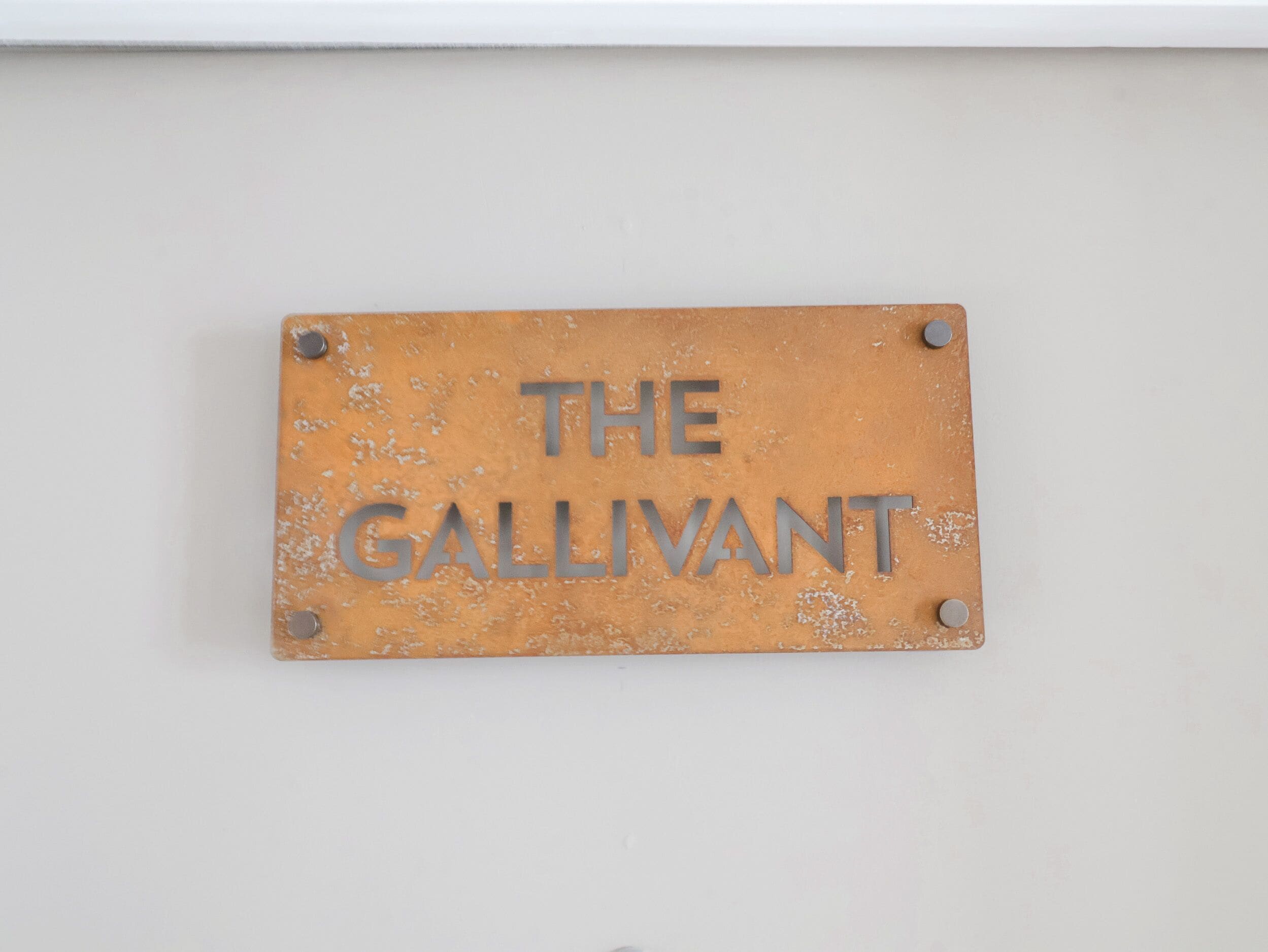 Kulunut metallilaatta, jossa on kaiverrus ”THE GALLIVANT”, on kiinnitetty valkoiseen seinään.