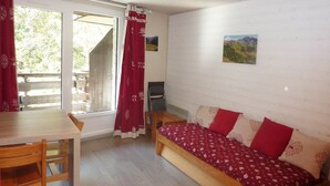 Une pièce avec un lit en bois, une table et des chaises. Il y a une fenêtre avec des rideaux.