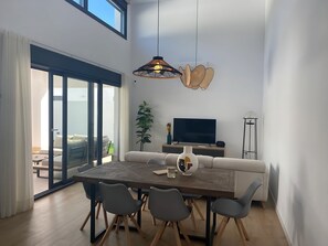 Ein modernes Wohnzimmer mit Esstisch, Stühlen, einer Couch, einem Fernseher und einer Stehlampe.
