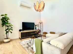 Ein modernes Wohnzimmer mit Flachbildfernseher, einer Couch, einem Couchtisch, einer Stehlampe und einem Topf mit Pflanze.
