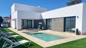 A modern house with a swimming pool, outdoor seating, and a car parked outside. - Villa Tres Mares - Extraordinary accommodation. (Poblado de Sancti Petri)