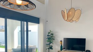 A modern living room with a wooden dining table, a sofa, a TV, and a large window. - Villa Tres Mares - Extraordinary accommodation. (Poblado de Sancti Petri)