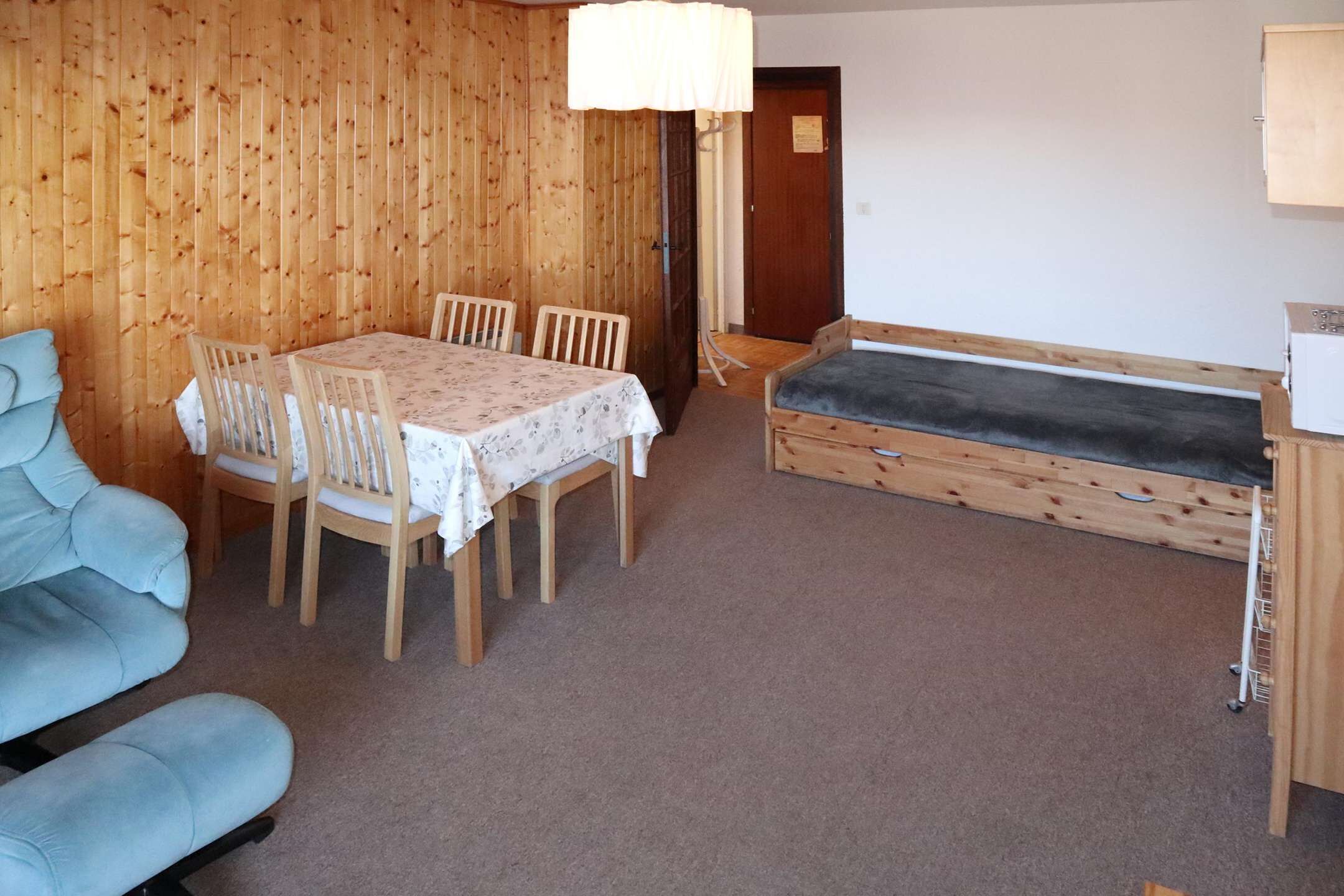 Ein Zimmer mit Holzwand, einem Esstisch mit Stühlen, einer Couch und einem kleinen Holzschrank.