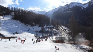 A ski resort with a large building, likely a lift station or lodge, surrounded by snow-covered mountains and trees. - Départ Skis aux Pieds (LES ORRES 1650)
