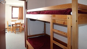 A bunk bed with a red mattress, a wooden desk, and a chair in a room with carpeted flooring. - Départ Skis aux Pieds (LES ORRES 1650)