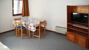A small room with a wooden table and chairs, a television on a wooden stand, and a radiator on the wall. - Départ Skis aux Pieds (LES ORRES 1650)