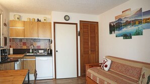 A compact kitchen with wooden cabinets, a white dishwasher, and a dining area with a wooden table and chairs. - Studio 6 Personnes Accès Direct aux Pistes (LES ORRES 1650)