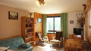 A cozy living room with a blue sofa, wooden bookshelf, and a dining table with chairs.