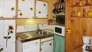 A compact kitchen with white cabinets featuring sunflower decals, a sink, a microwave, and a coffee maker.