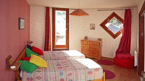 Un dormitorio con dos camas, un aparador de madera, un sillón de peluche rojo, una ventana y una puerta.