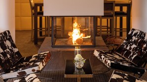 A room with a glass-top table, two patterned chairs, a whiteboard, and a fireplace with a visible fire. - HÔTEL À LA FERME (Osthouse)