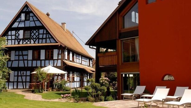 A traditional half-timbered house with a modern extension, a patio with lounge chairs, and a well-maintained garden. - HÔTEL À LA FERME (Osthouse)